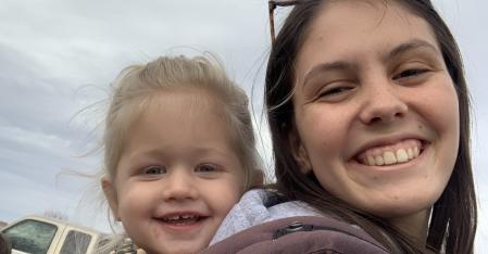 Au pair mit einem kleinen Mädchen in einer Rückentrage, lächelnd