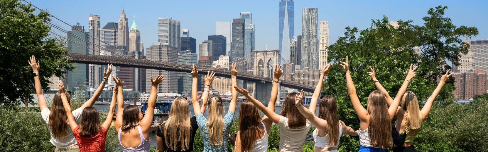 Große Gruppe an Au Pairs heben die Arme in die Luft mit der Skyline Manhattans im Hintergrund