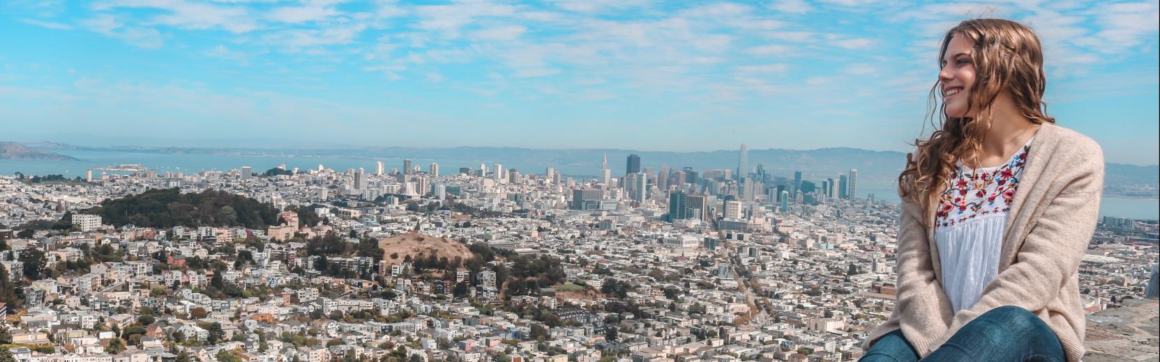 Au pair sitzt auf einer Mauer und schaut runter auf das Panorama einer Stadt in den USA