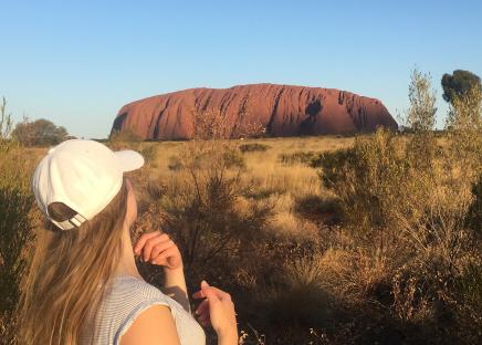 Au pair, mit dem Rücken zur Kamera, schaut auf den Uluru in der Ferne